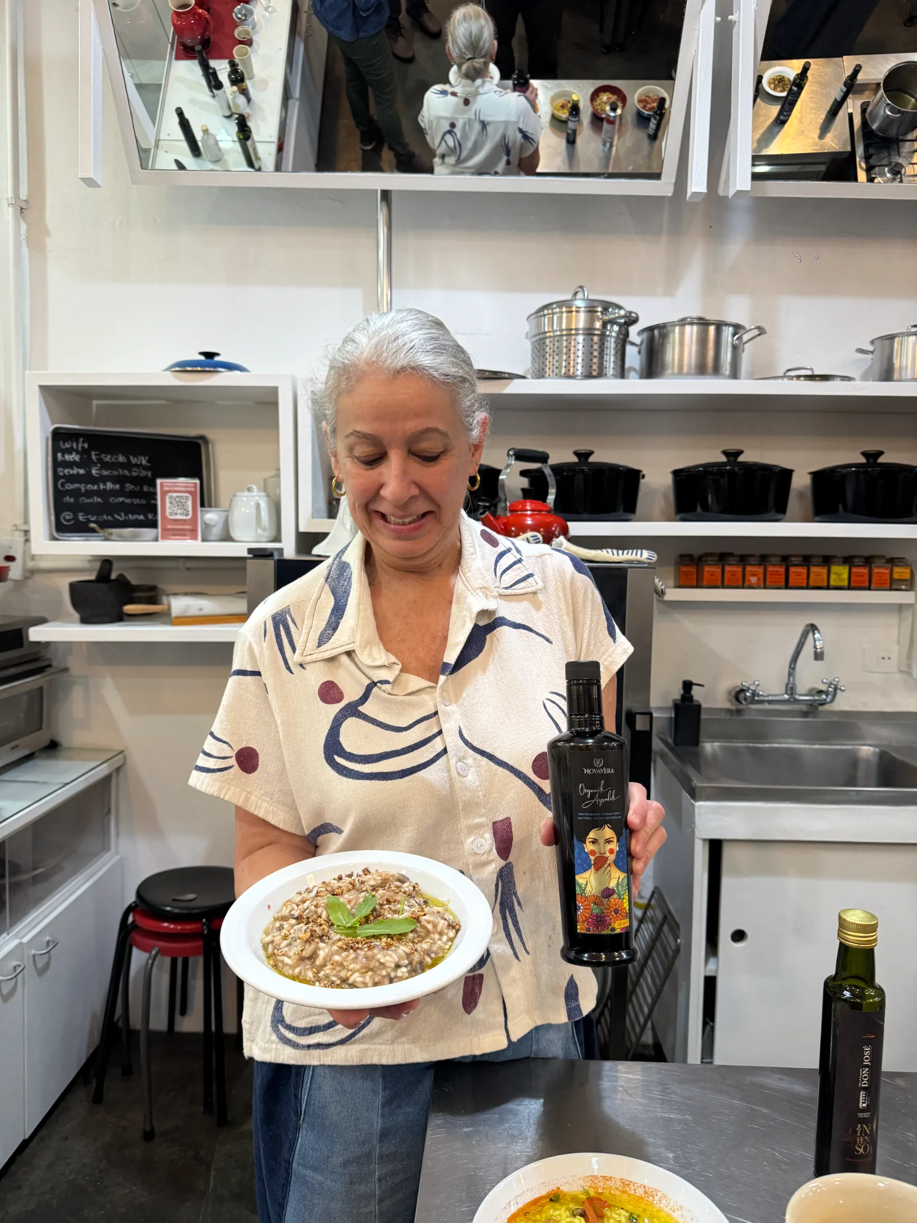 Participante apresenta um prato e uma garrafa de azeite durante a atividade prática na cozinha da Escola Wilma Kövesi